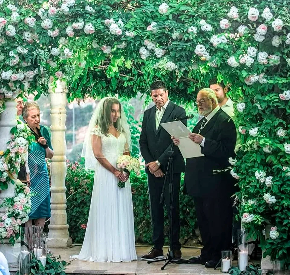A wedding ceremony beneath a canopy of greenery and roses