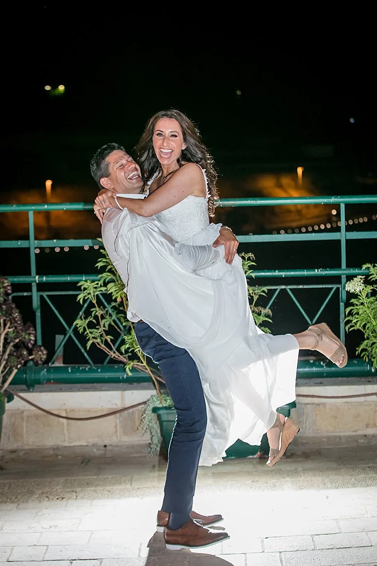 A laughing groom lifting his bride during their wedding celebration